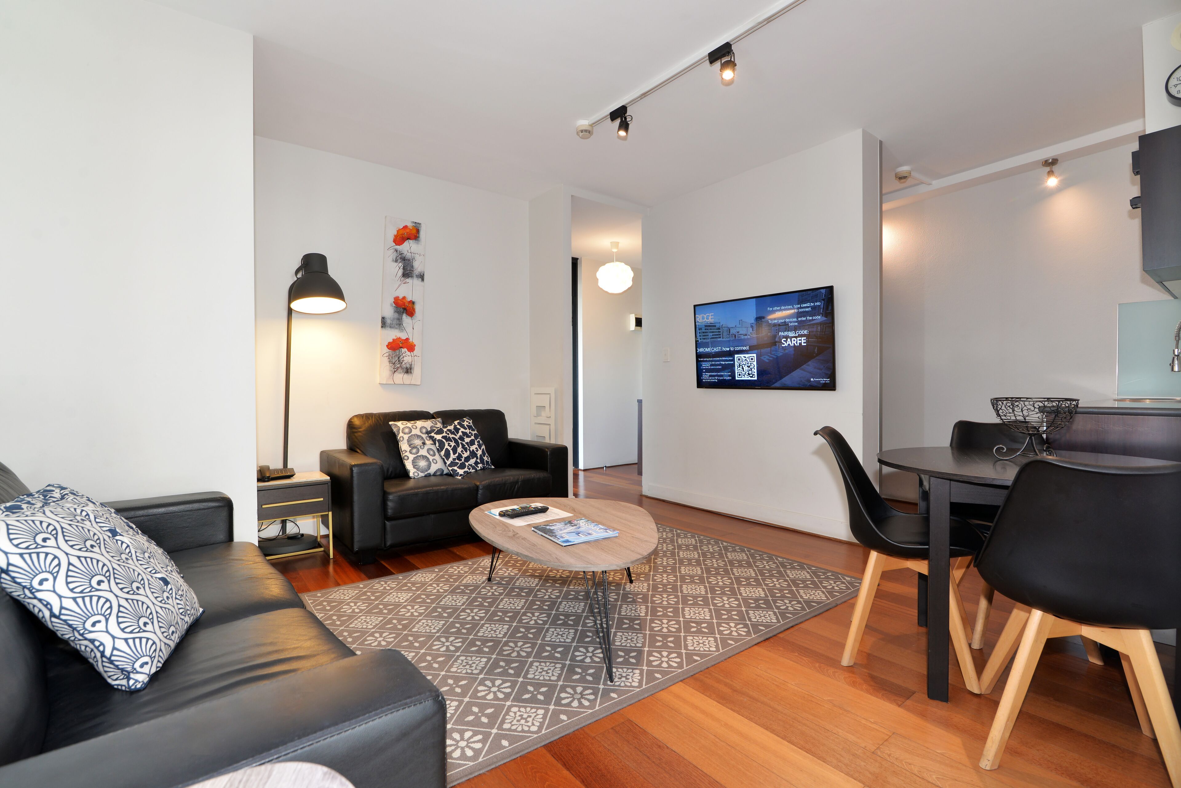 Una sala de estar moderna con un sofá negro, una mesa de centro y una zona de comedor con mesa y sillas.