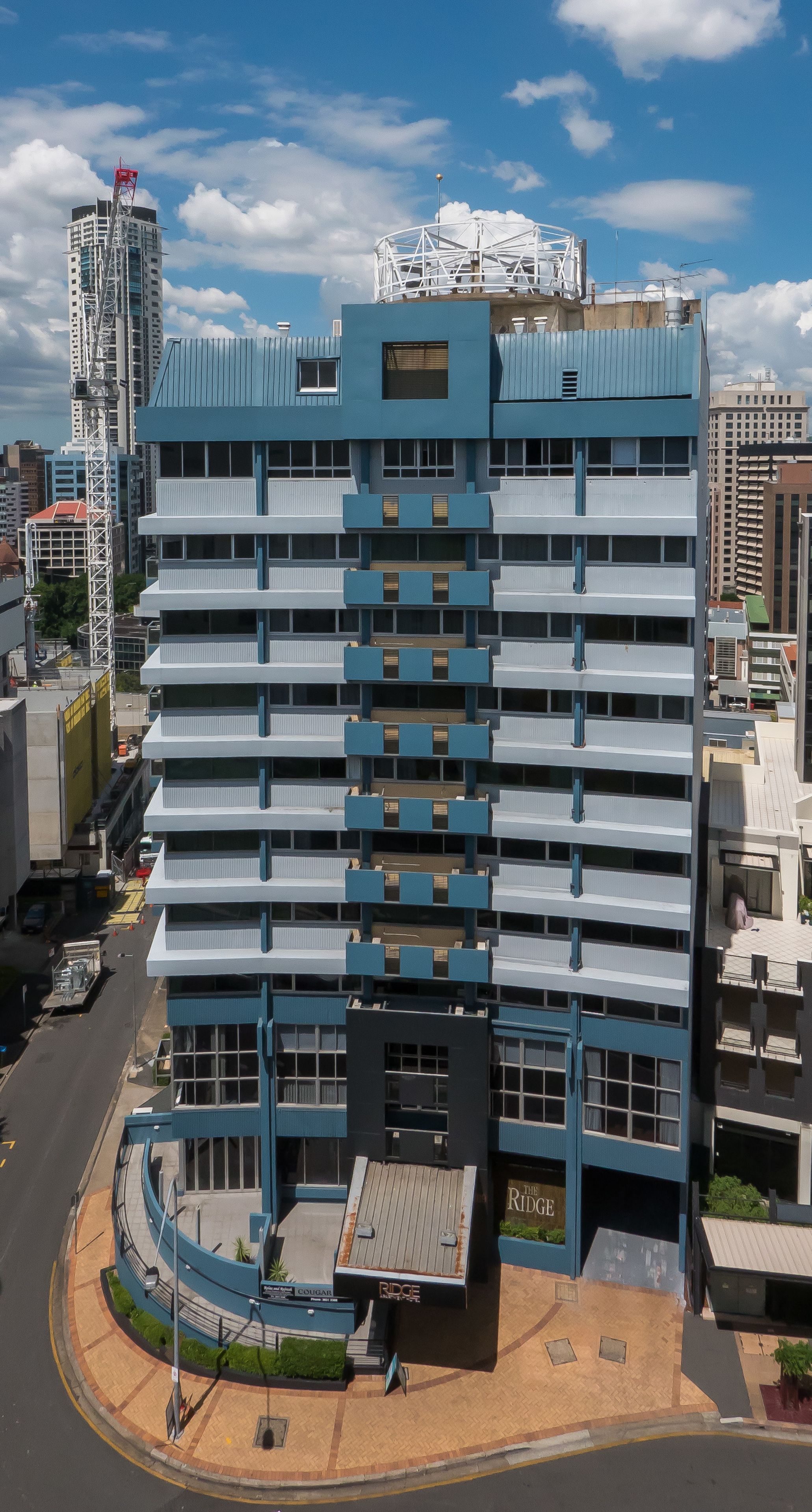 A multi-story hotel with a blue and white facade, a rooftop terrace, and a sign reading "The Ridge".