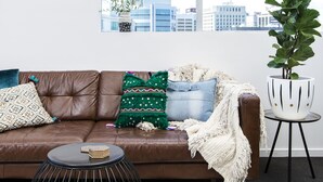 A brown leather sofa with patterned cushions, a round black metal side table, and a white potted plant. - The Ridge Apartment Hotel (Spring Hill)