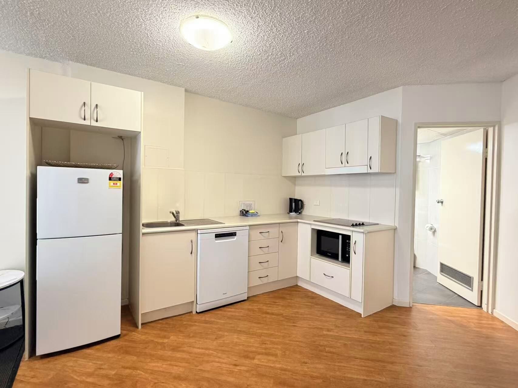 Una cocina compacta con armarios blancos, lavavajillas integrado, microondas y refrigerador.