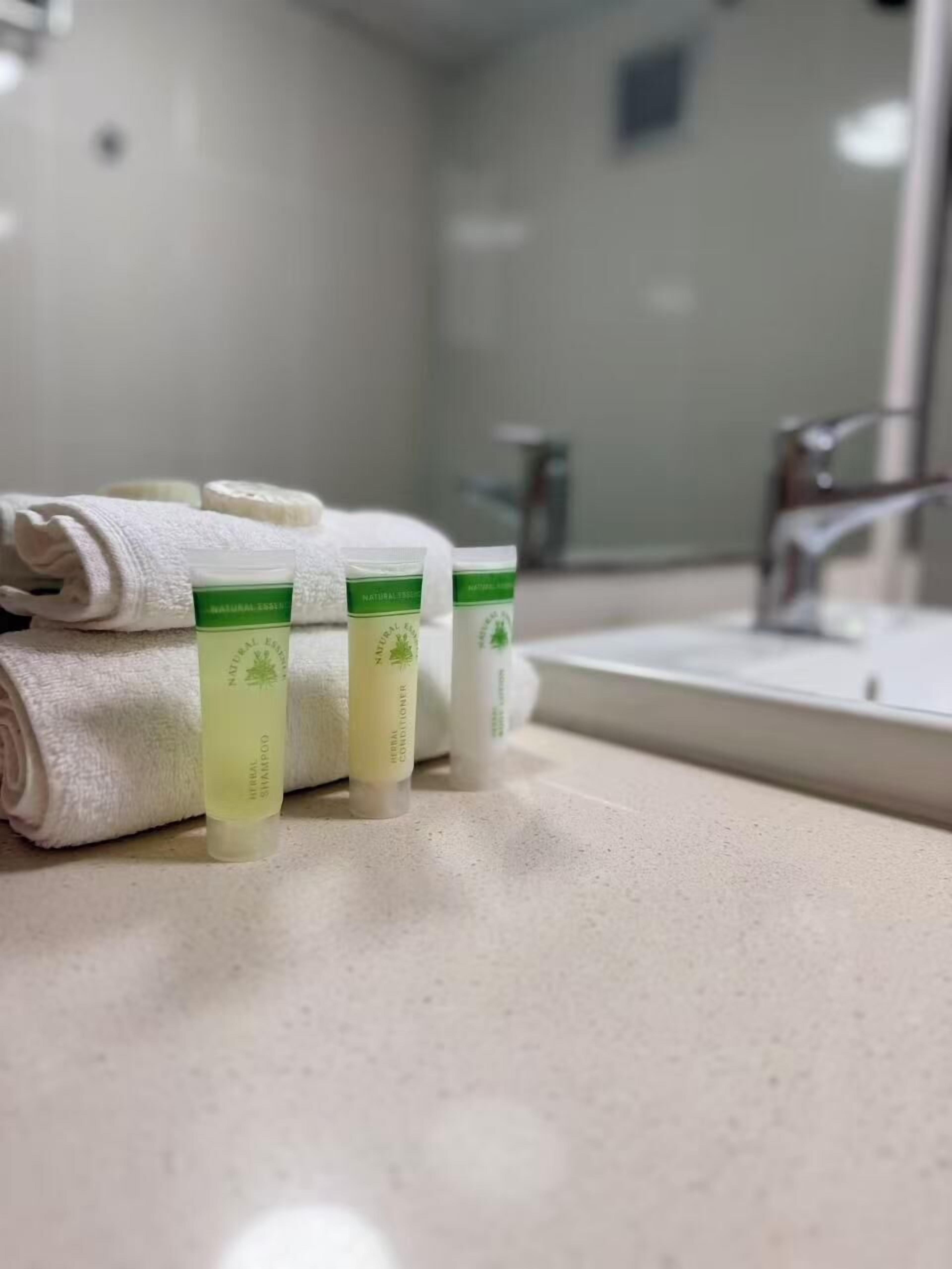 A bathroom with a white sink, a mirror, and three bottles of natural shampoo and conditioner on the counter.