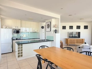 Une cuisine moderne avec des meubles blancs, un plan de travail noir et une table à manger en bois, accompagnée de chaises.