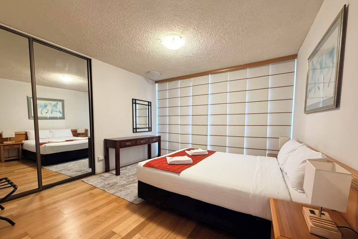 A hotel room with a bed, bedside table, desk, chair, and a large mirror.