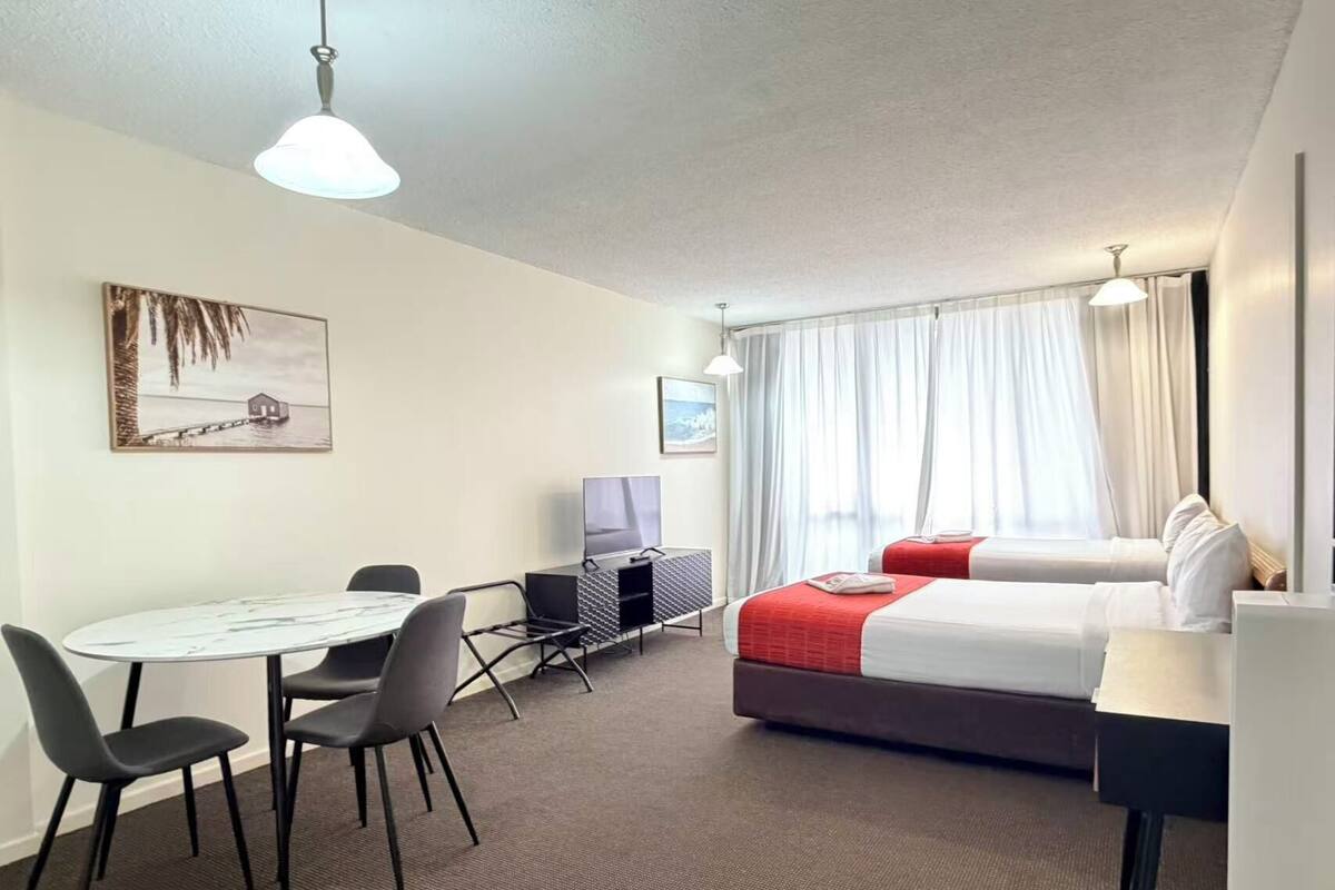 A hotel room with a bed, a desk, a TV, and a painting on the wall.