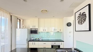 Une cuisine moderne avec des meubles blancs, un plan de travail noir, un évier en acier inoxydable, un four à micro-ondes et une bouilloire.