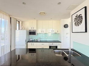 A modern kitchen with white cabinets, a black countertop, a stainless steel sink, a microwave, and a kettle. - The Summit Apartments (Spring Hill)