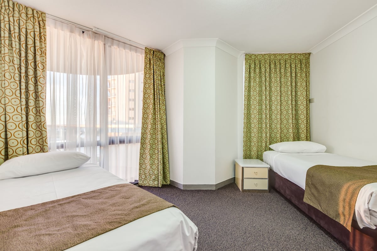Habitación de hotel con dos camas, mesitas de noche y una ventana con cortinas translúcidas.