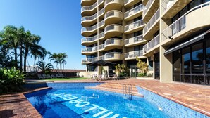 Un hotel con piscina, mobiliario exterior y un edificio de varios pisos con balcones.
