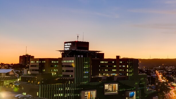 Un edificio de hospital con un letrero que indica el Hospital Infantil Lady Clinton, rodeado de otros edificios y un paisaje urbano al anochecer.