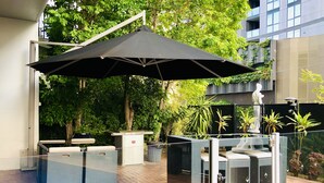 Un área de patio al aire libre con un parasol negro grande, mobiliario de mimbre y plantas en macetas.
