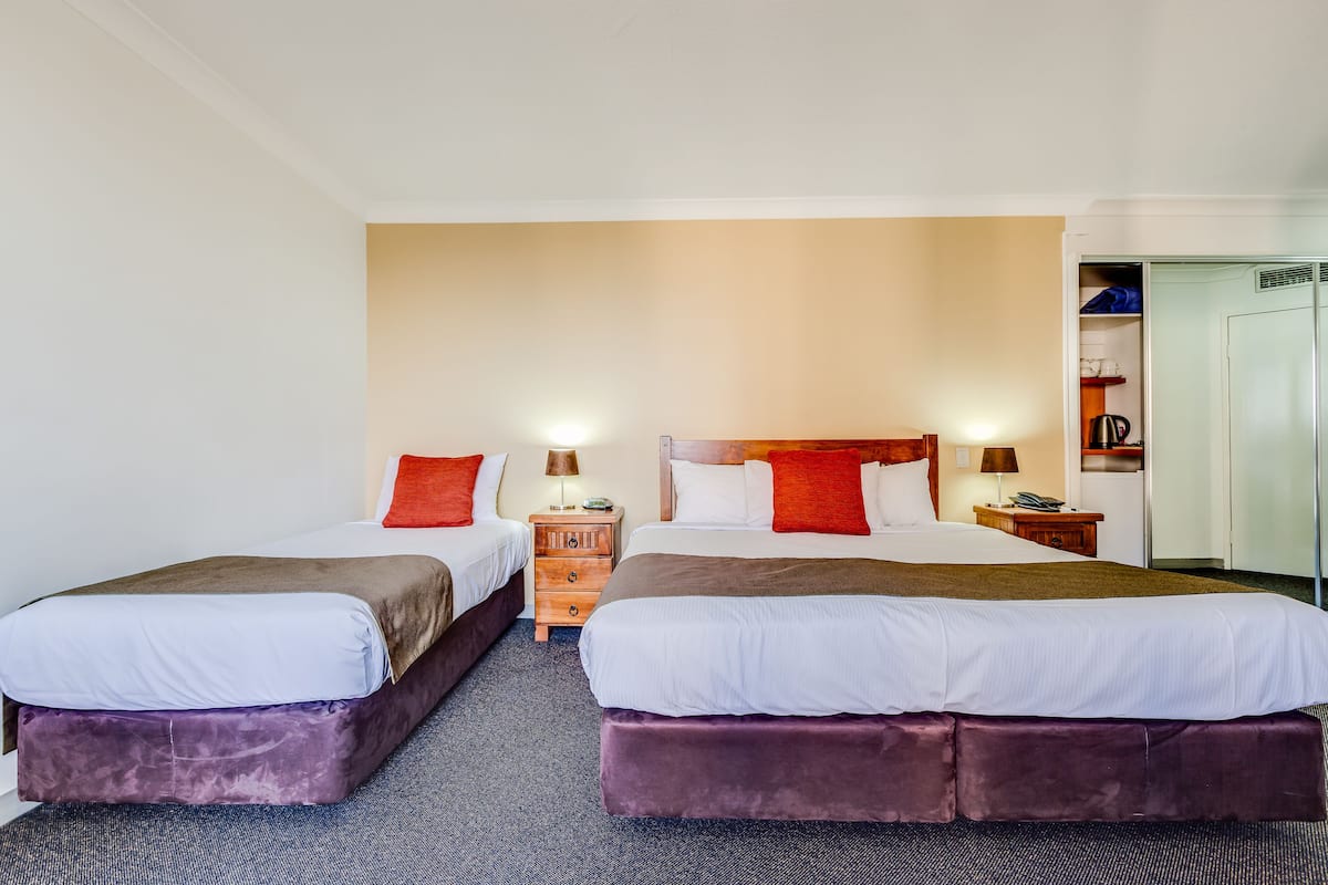 Habitación de hotel con dos camas, un armario y un escritorio con lámpara.