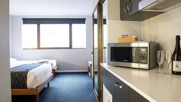 Quarto de hotel com cama, micro-ondas, garrafa de vinho e uma pequena mesa.