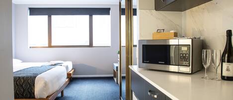 A hotel room with a bed, a microwave, a wine bottle, and a small table.
