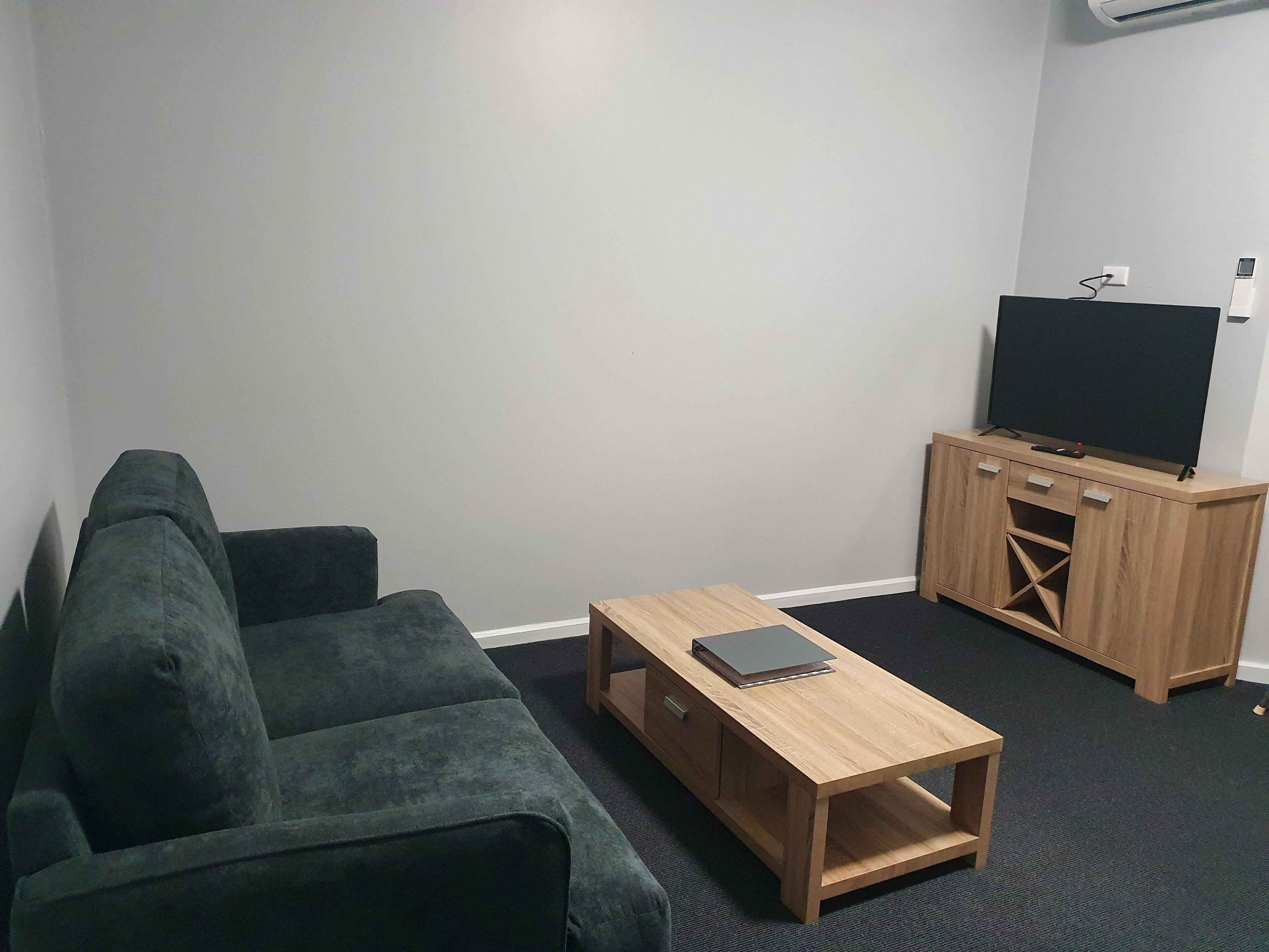 A living room with a green sofa, a wooden coffee table, and a TV on a wooden stand.