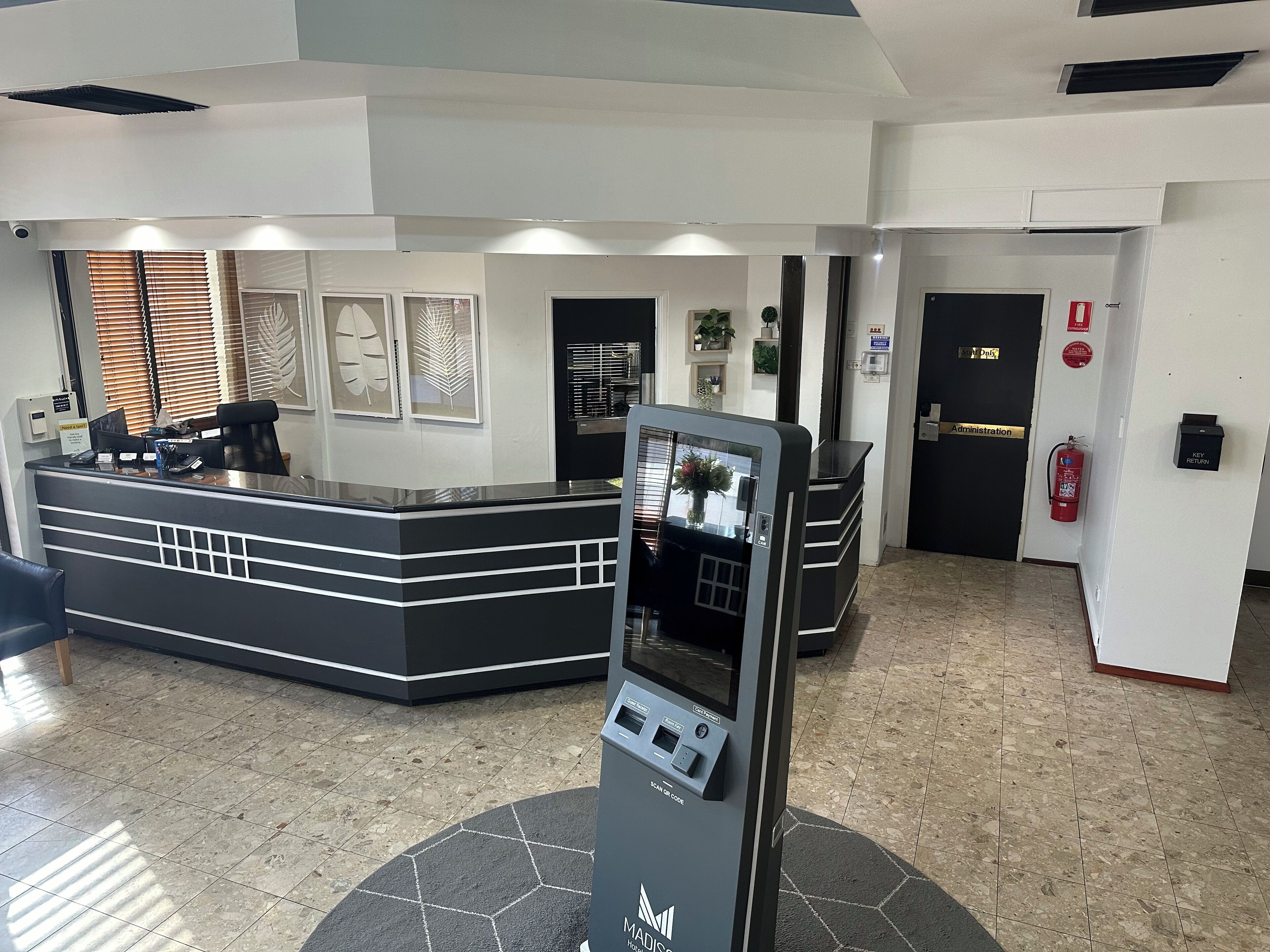 A reception area with a black reception desk, a self-service kiosk, and a fire extinguisher mounted on the wall.