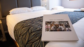 Una habitación de hotel con una cama bien hecha, un libro titulado 'THIS IS CANBERRA' y una manta decorativa.