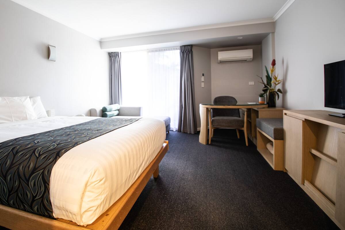 A hotel room with a large bed, a desk, a chair, and a television.