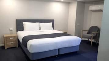 A neatly arranged hotel room with a large bed, a bedside table, a chair, and an air conditioning unit.