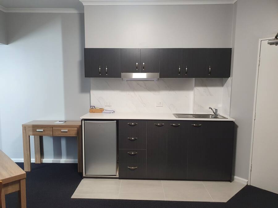 A compact kitchen with dark cabinets, a built-in dishwasher, and a white countertop.