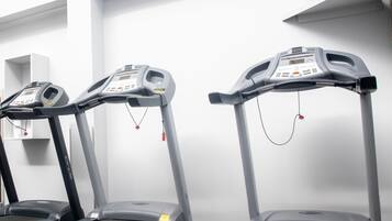 Three treadmills in a gym with a white wall and a television mounted above.