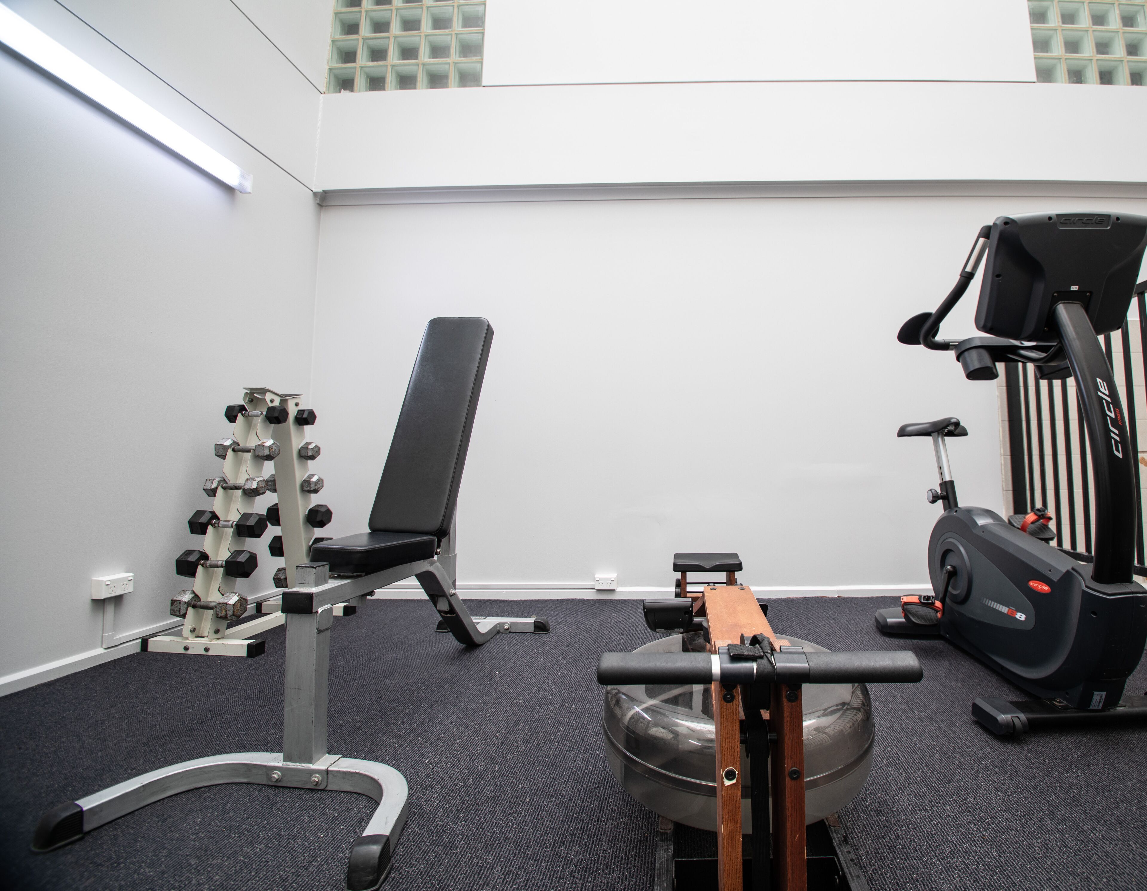 A gym with a bench press, dumbbells, and an elliptical machine.