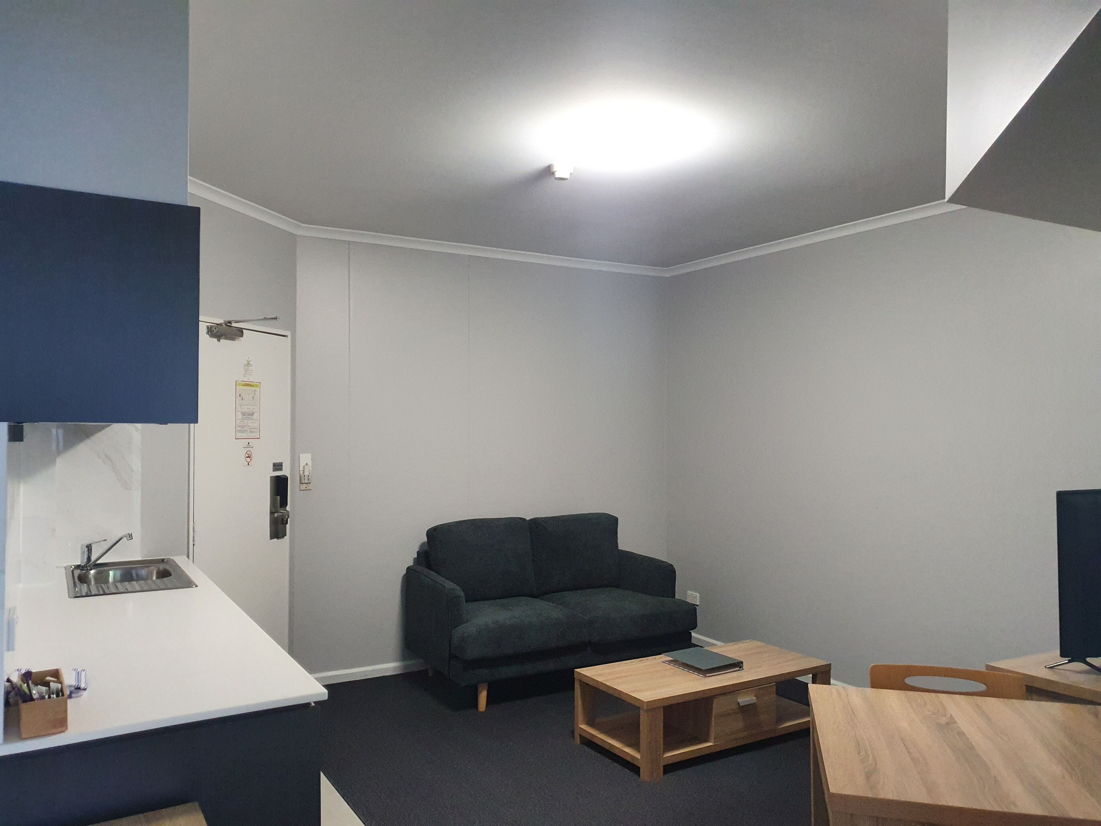 Un petit salon moderne avec un canapé vert foncé, une table basse en bois et un plan de travail blanc doté d’un évier.