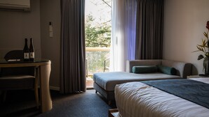 Habitación de hotel con una cama, un escritorio con dos botellas, una silla y vistas a árboles por la ventana.