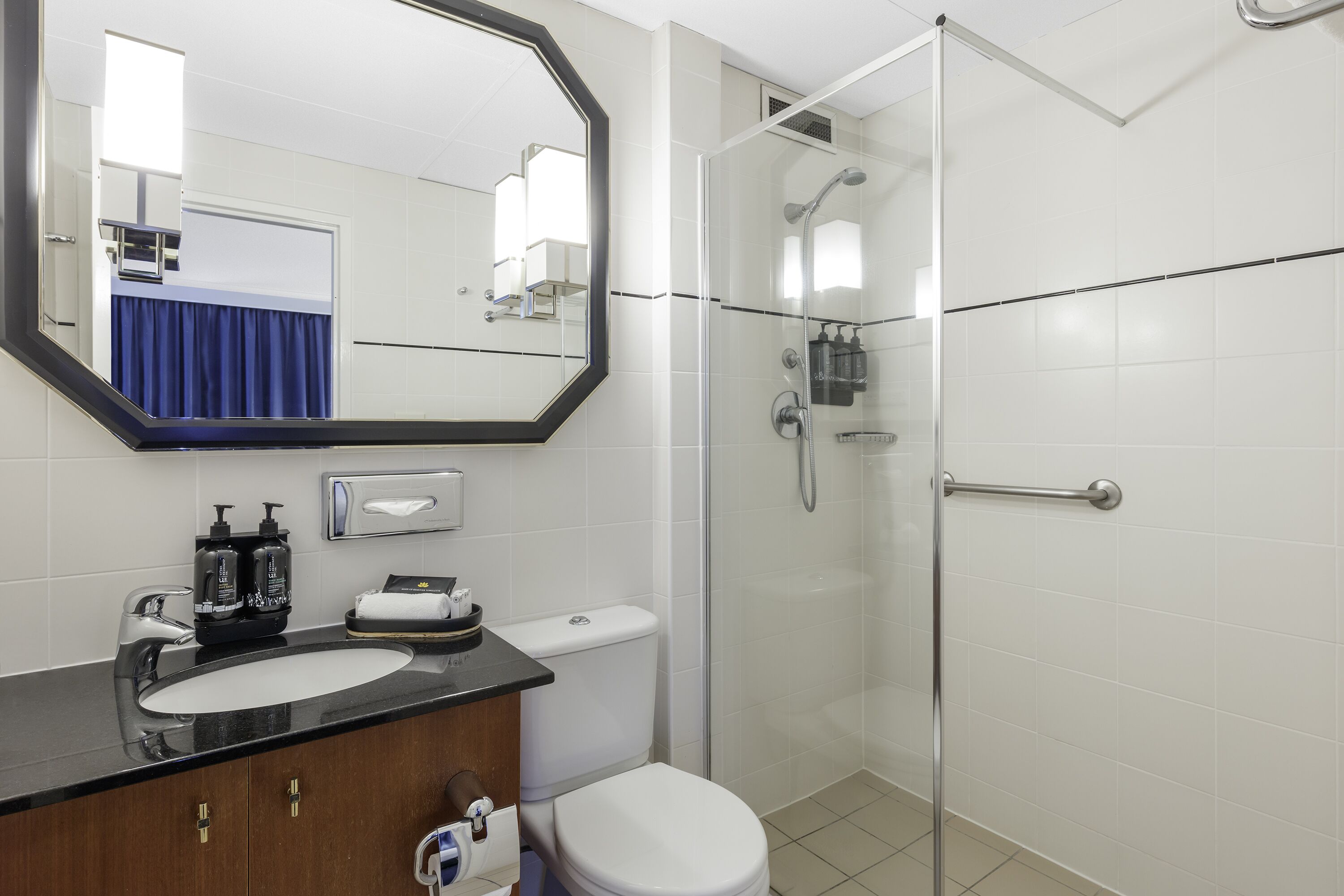 A modern bathroom with a large mirror, a sink, a toilet, and a glass-enclosed shower.