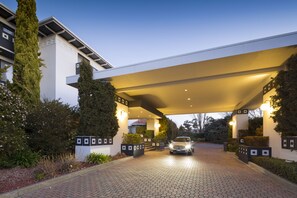 A hotel entrance with a covered driveway, a car parked in front, and a well-maintained garden area. - Ramada by Wyndham Diplomat Canberra (Griffith)