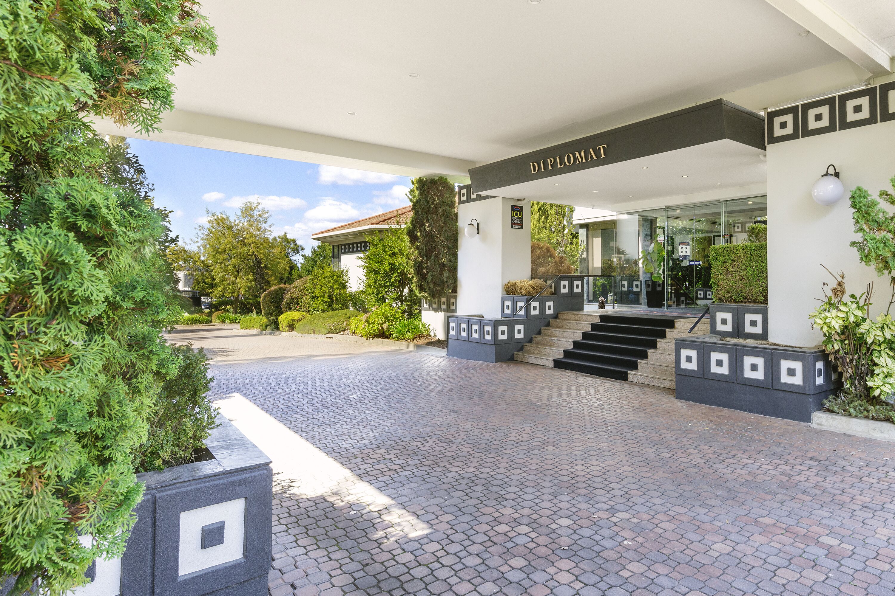 Una entrada de edificio moderna con un letrero que dice "Diplomat" y un camino pavimentado que conduce a la entrada.