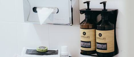 Un baño con encimera negra, lavamanos blanco y dos botellas de loción corporal etiquetadas como "Appelles".