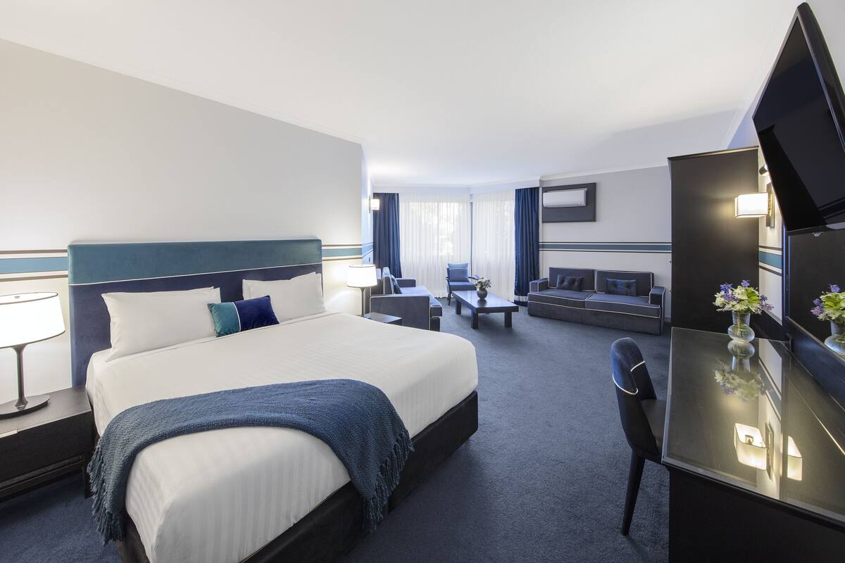 Ein Hotelzimmer mit einem großen Bett, einem Schreibtisch mit Stuhl, einer Couch und einem Fernseher.