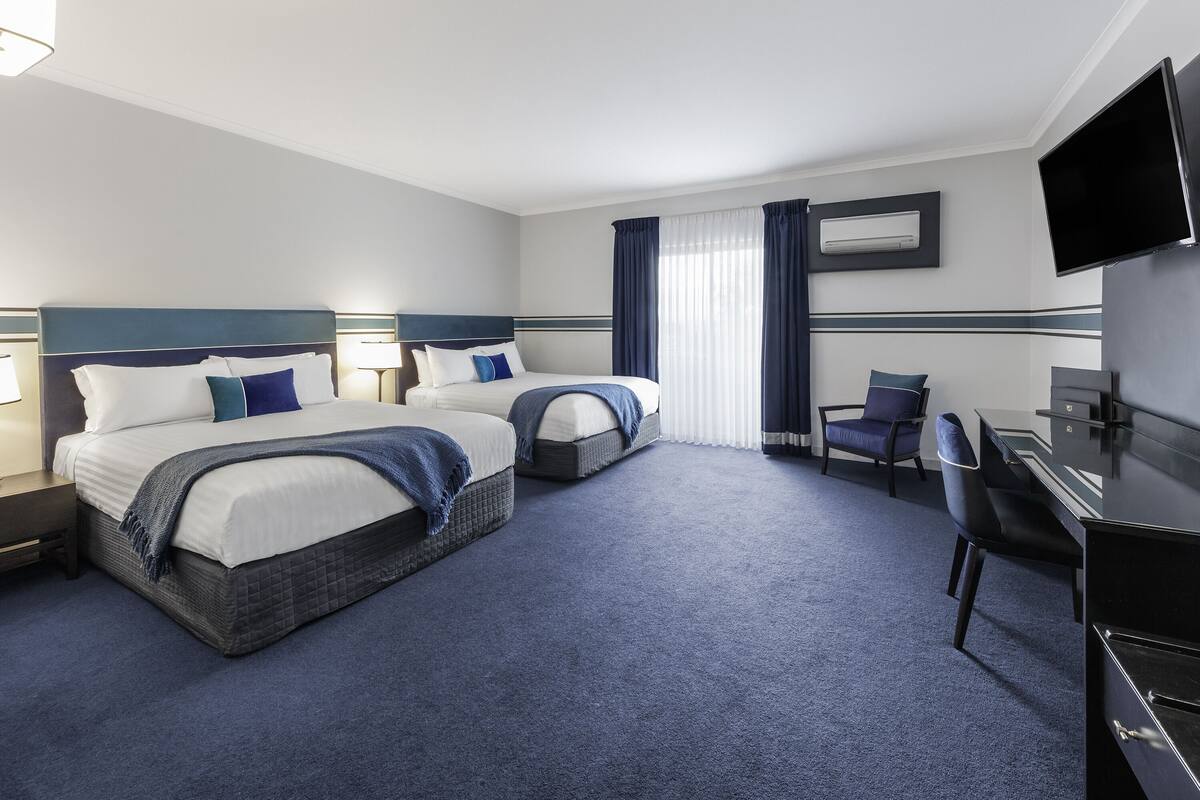 Ein Hotelzimmer mit zwei Betten, einem Schreibtisch, einem Stuhl, einem Fernseher und einem Fenster mit Vorhängen.