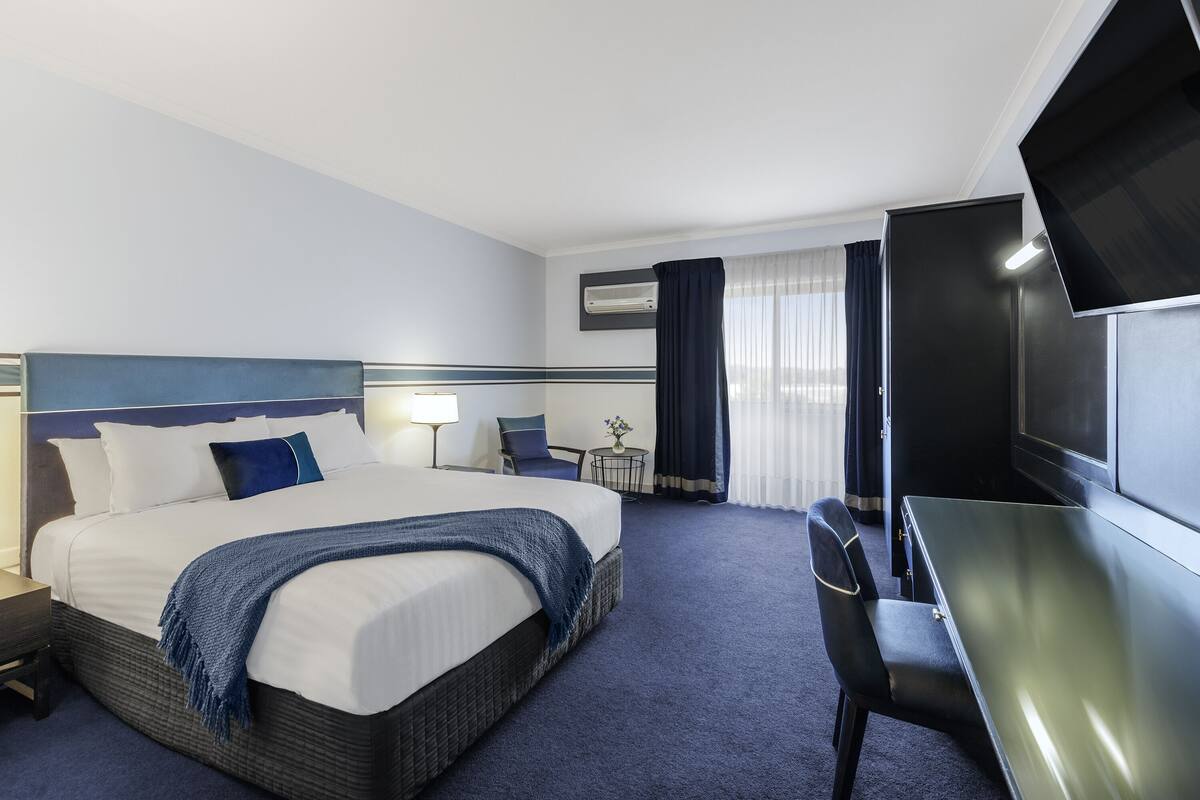 Ein Hotelzimmer mit einem großen Bett, einem Schreibtisch, einem Stuhl, einem Fernseher und einer Klimaanlage.