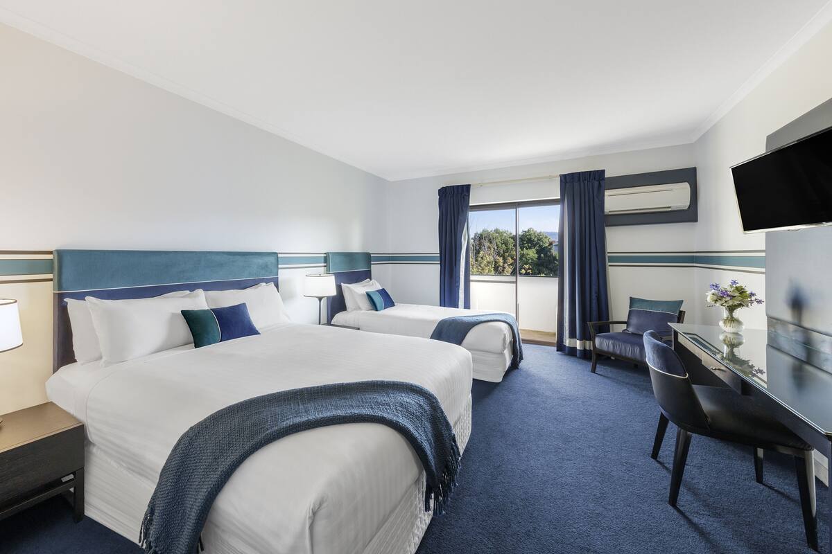 Ein Hotelzimmer mit zwei Betten, einem Schreibtisch, einem Stuhl, einem Fernseher und einem Fenster mit Vorhängen.
