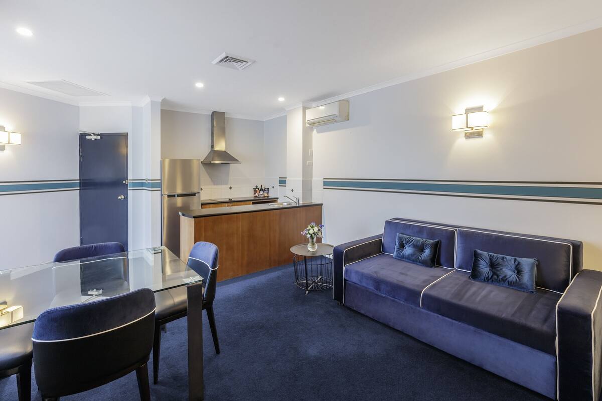Ein modernes Hotelzimmer mit einem Glastisch, einer Sitzecke und einer kleinen Küchenzeile.