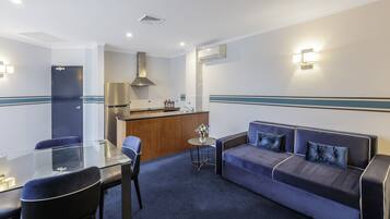 Ein modernes Hotelzimmer mit einem Glastisch, einer Sitzecke und einer kleinen Küchenzeile.
