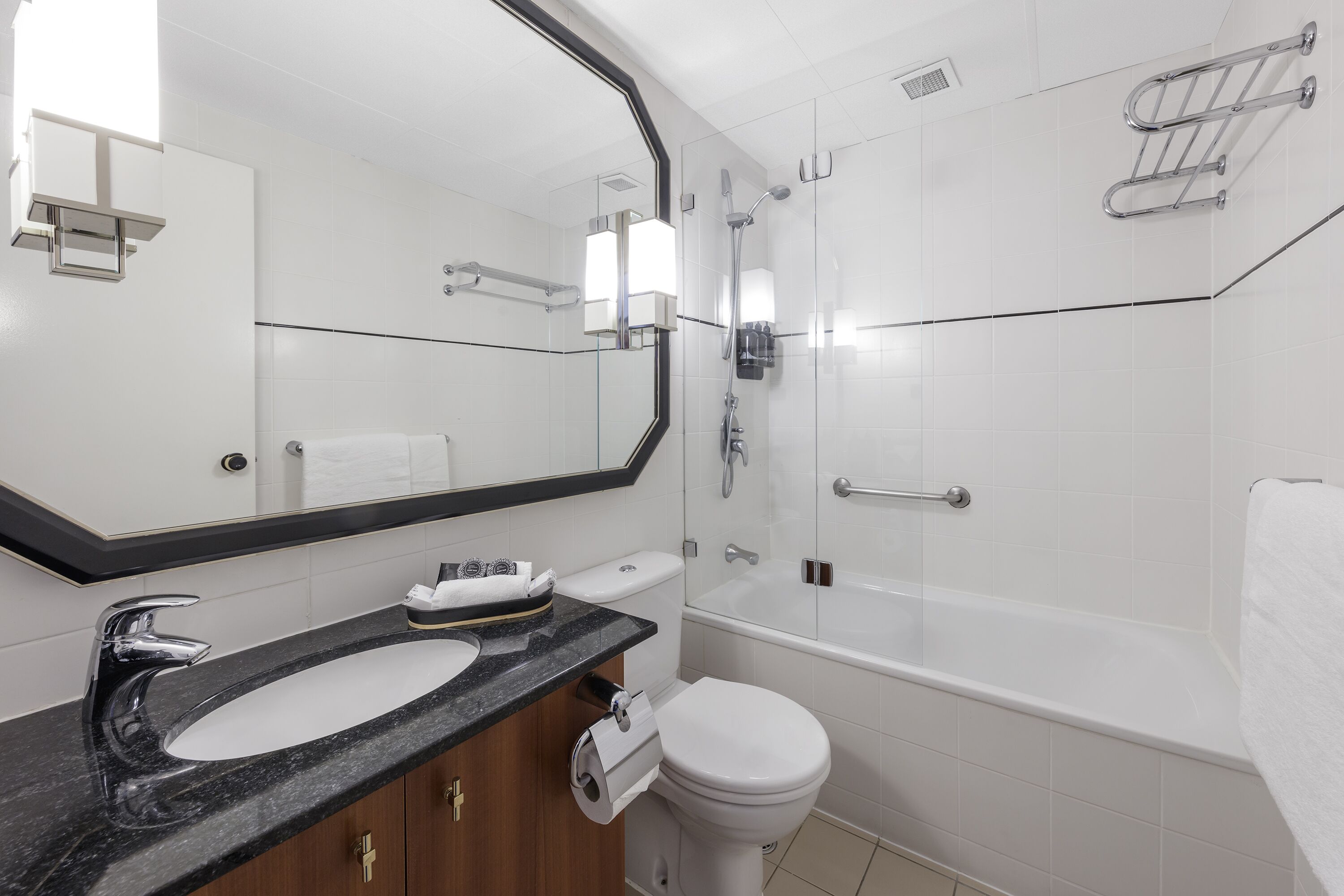 Un baño moderno con un lavabo de mármol negro, un inodoro blanco, ducha con mampara de vidrio y un espejo grande.