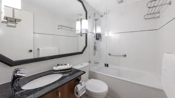 Un baño moderno con un lavabo de mármol negro, un inodoro blanco, ducha con mampara de vidrio y un espejo grande.