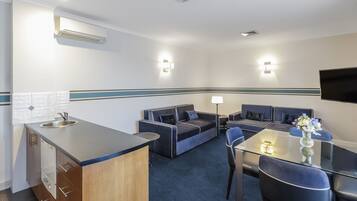 Ein kompaktes Hotelzimmer mit Küchenzeile, einer Couch, einem Esstisch und einem Flachbildfernseher.
