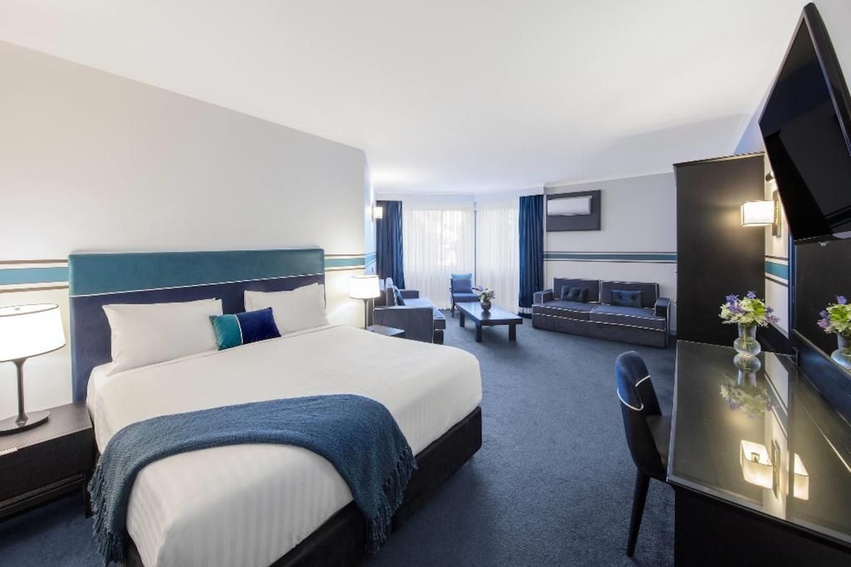 A hotel room with a large bed, a desk, a chair, a TV, and a sofa.