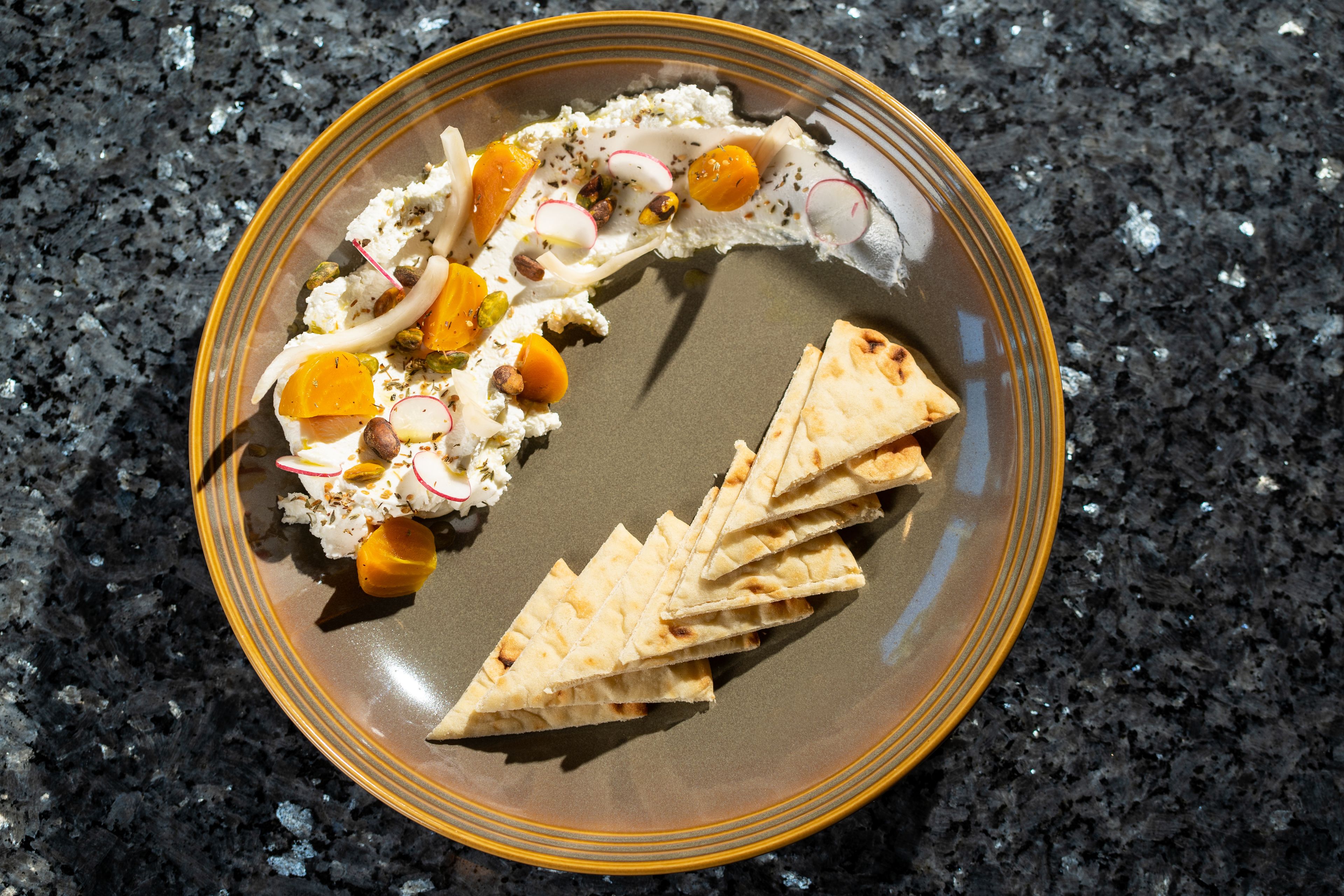 A plate with flatbread, cheese, and vegetables on a dark granite countertop.