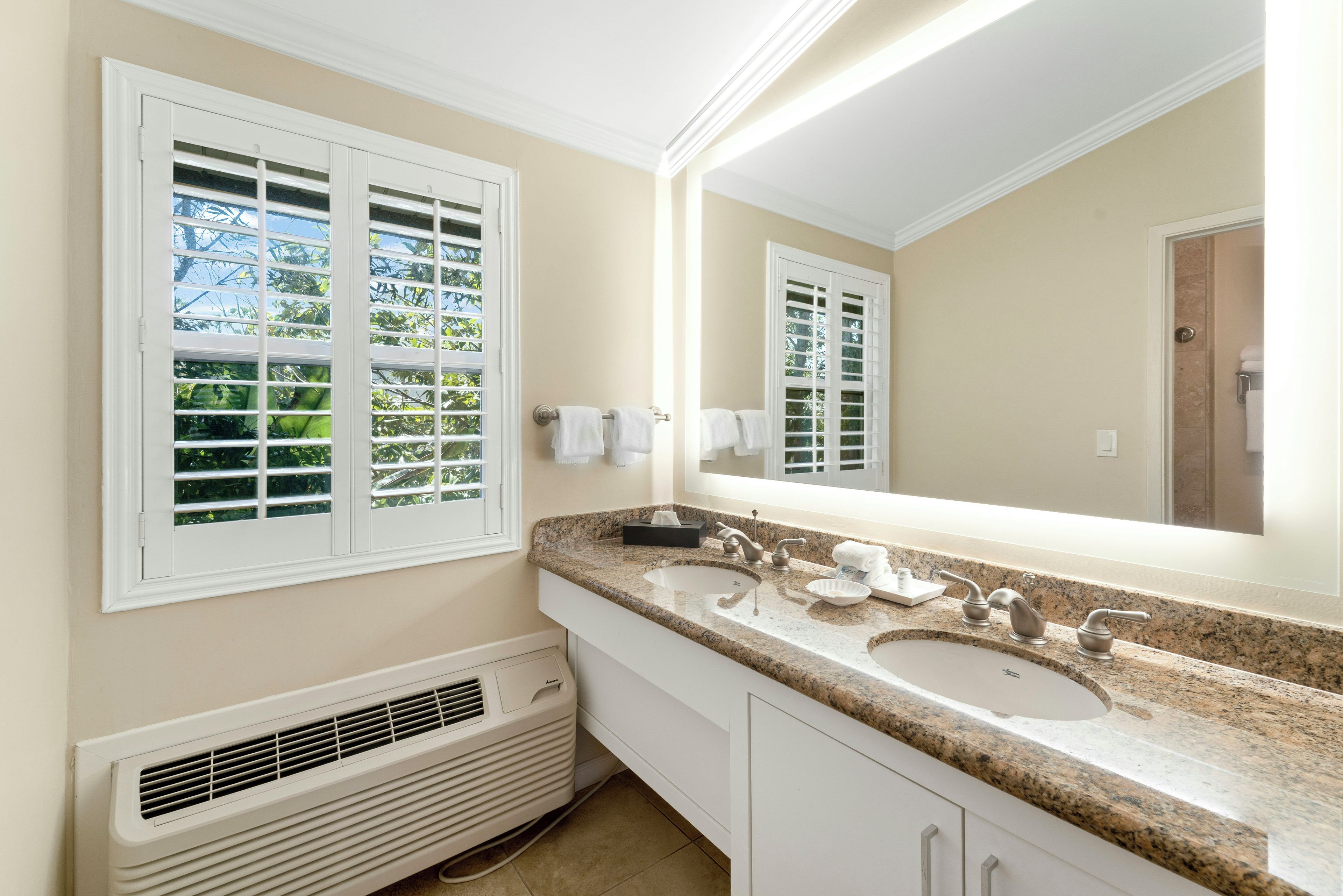 A bathroom with two sinks, a large mirror, and a window with blinds.