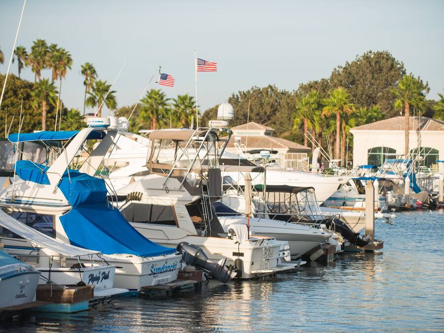 A marina with multiple boats docked, some with blue covers, and a few with American flags.