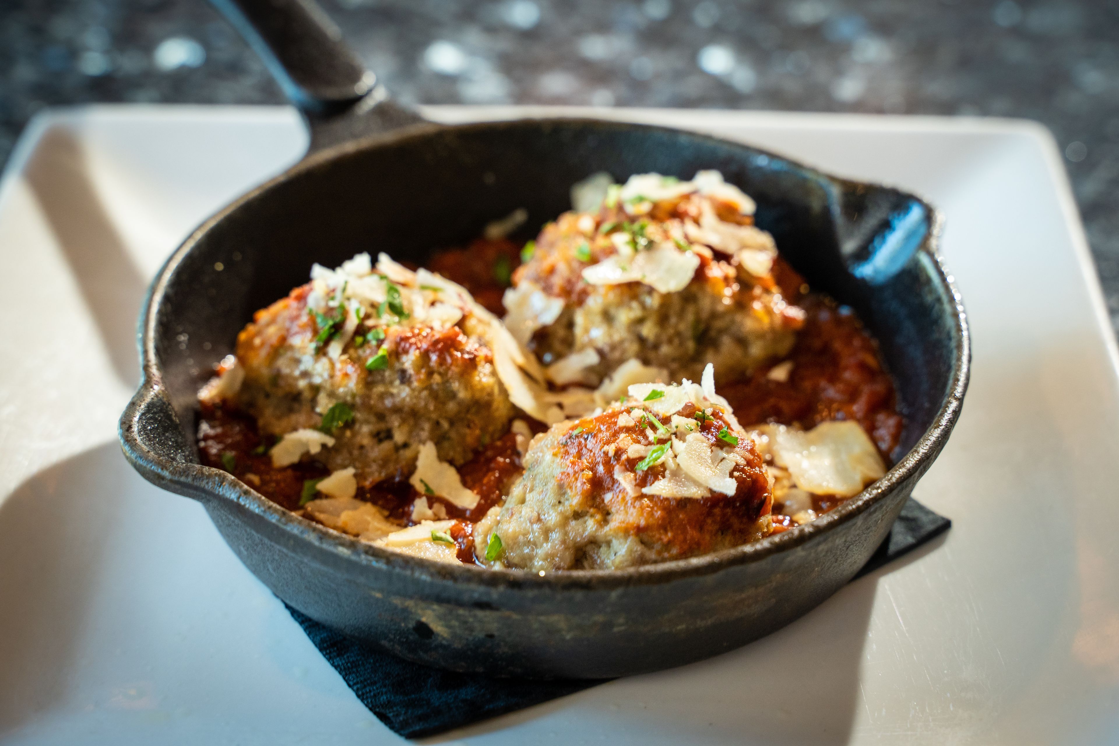 A skillet with meatballs in tomato sauce, garnished with cheese and herbs.