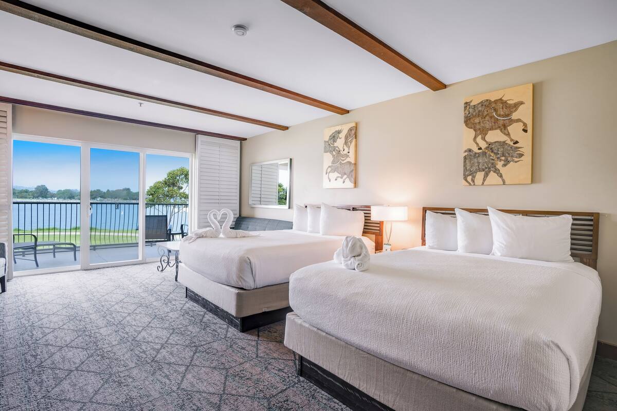 A hotel room with two beds, a balcony with a view, and artwork on the walls.