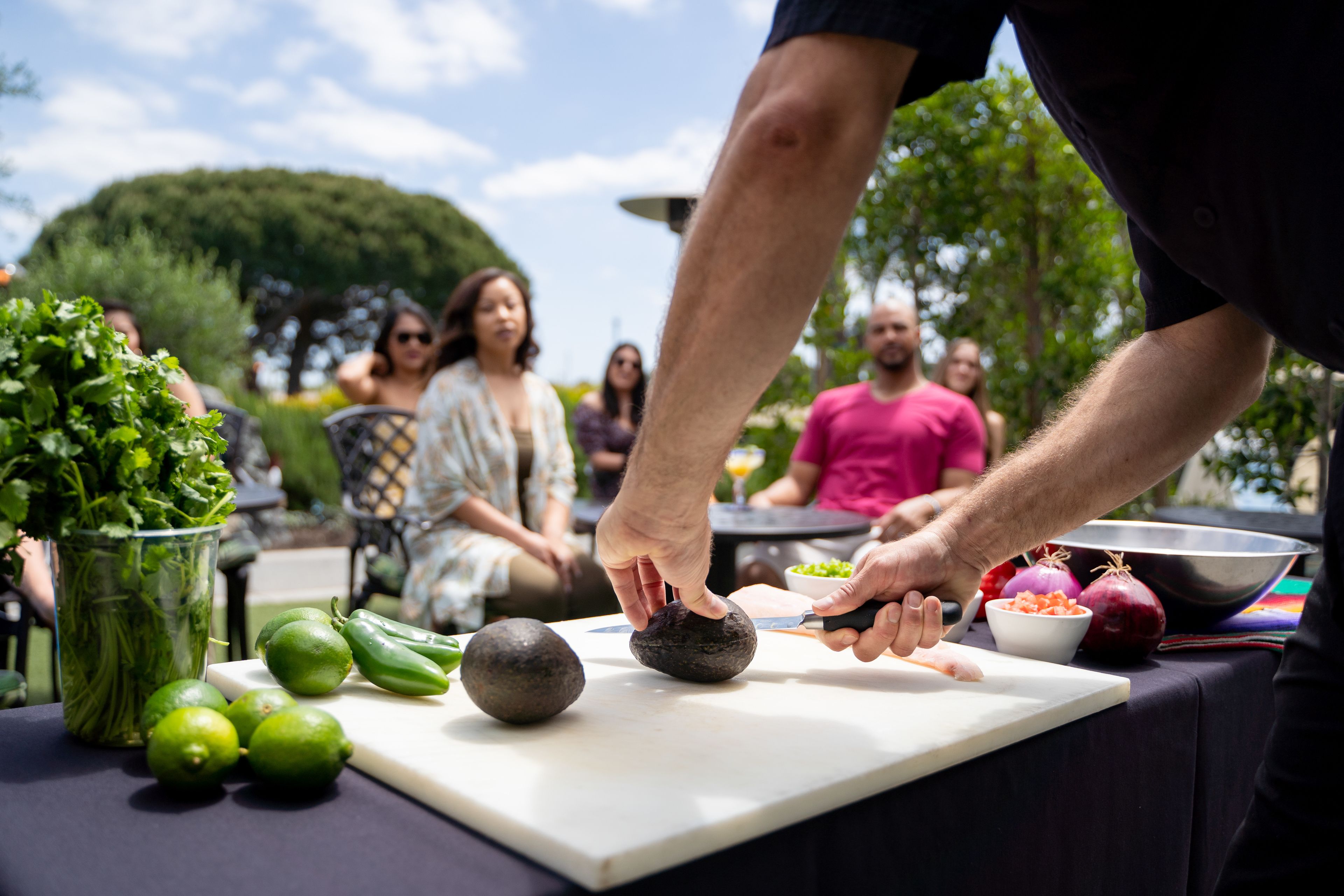 Una persona preparando comida al aire libre, con una tabla de cortar, verduras y un bol.