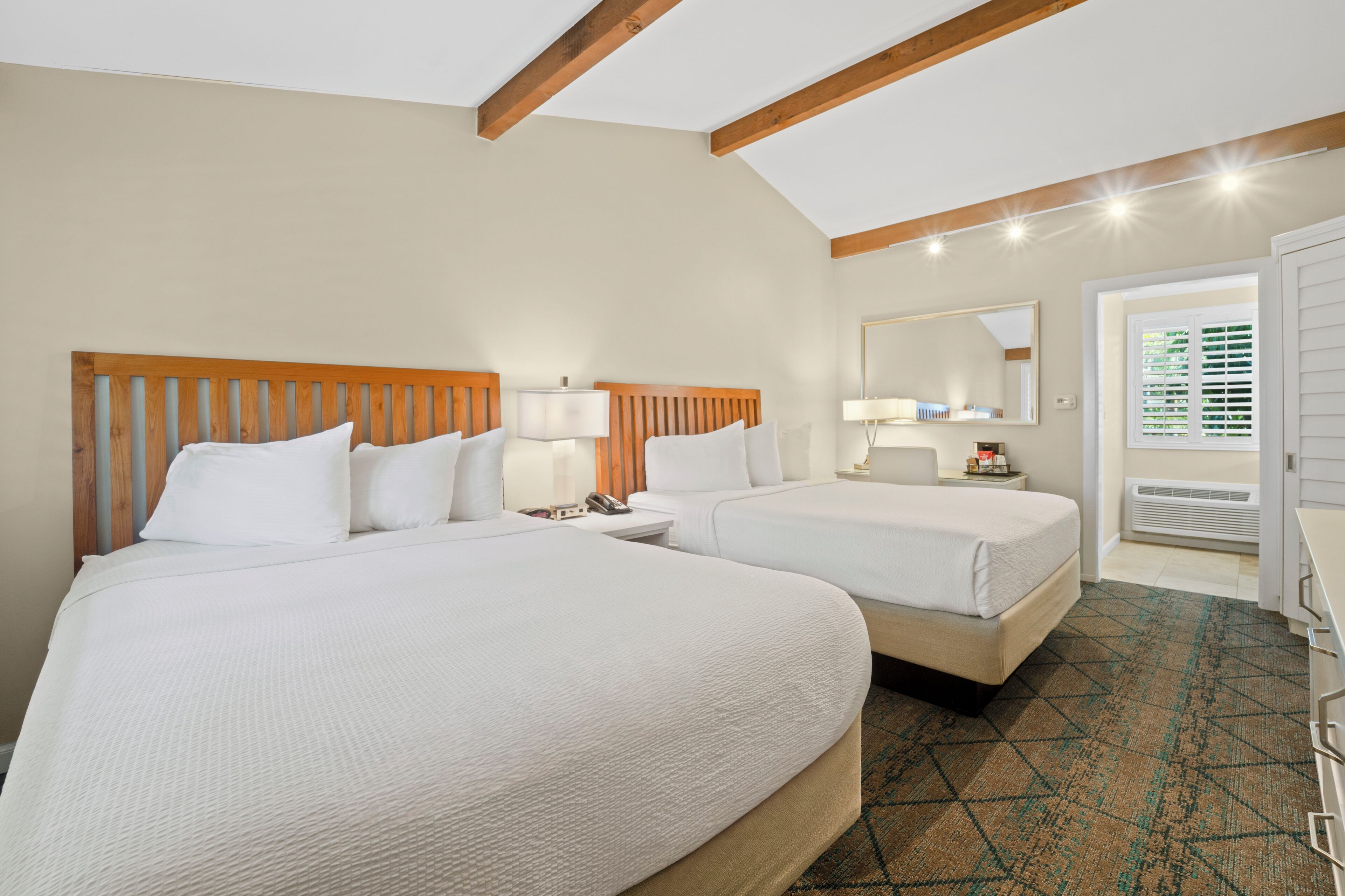A hotel room with two beds, a nightstand, a lamp, a mirror, and a door leading to a balcony.