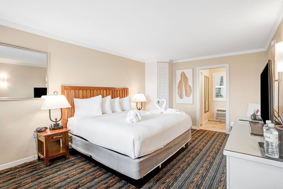 A hotel room with a large bed, two bedside tables with lamps, a desk with a chair, and a television.