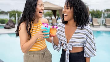 Two people holding drinks by a poolside.